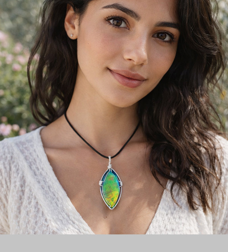 A woman with dark hair and a white blouse wearing a colourful green and yellow Ammolite silver wire-wrapped pendant from KORITE.